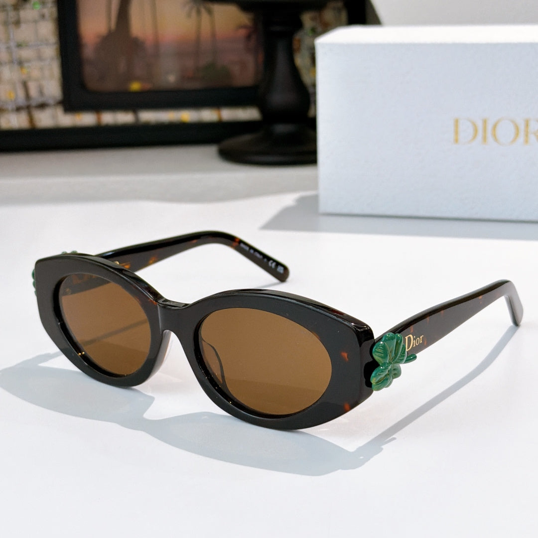 Dior sunglasses with black frames and tan tinted lenses, featuring a green flower detail on the side.