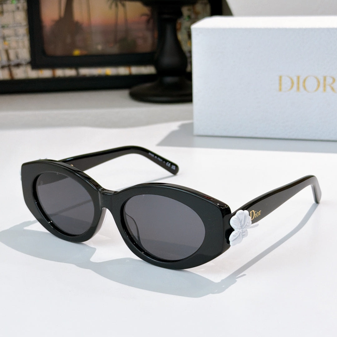 Dior sunglasses with black frames and dark lenses, with a white flower detail on the temple.