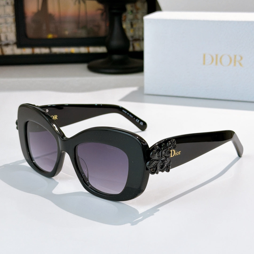Dior sunglasses with black frames, purple-tinted lenses, and dark floral temple detail