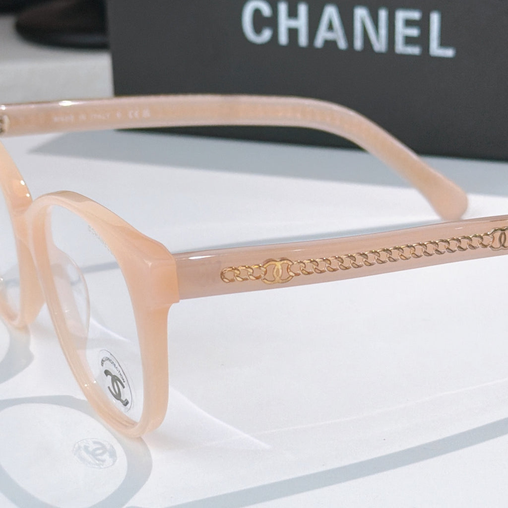 Light peach eyeglasses close-up with gold chain-style detail on the temple