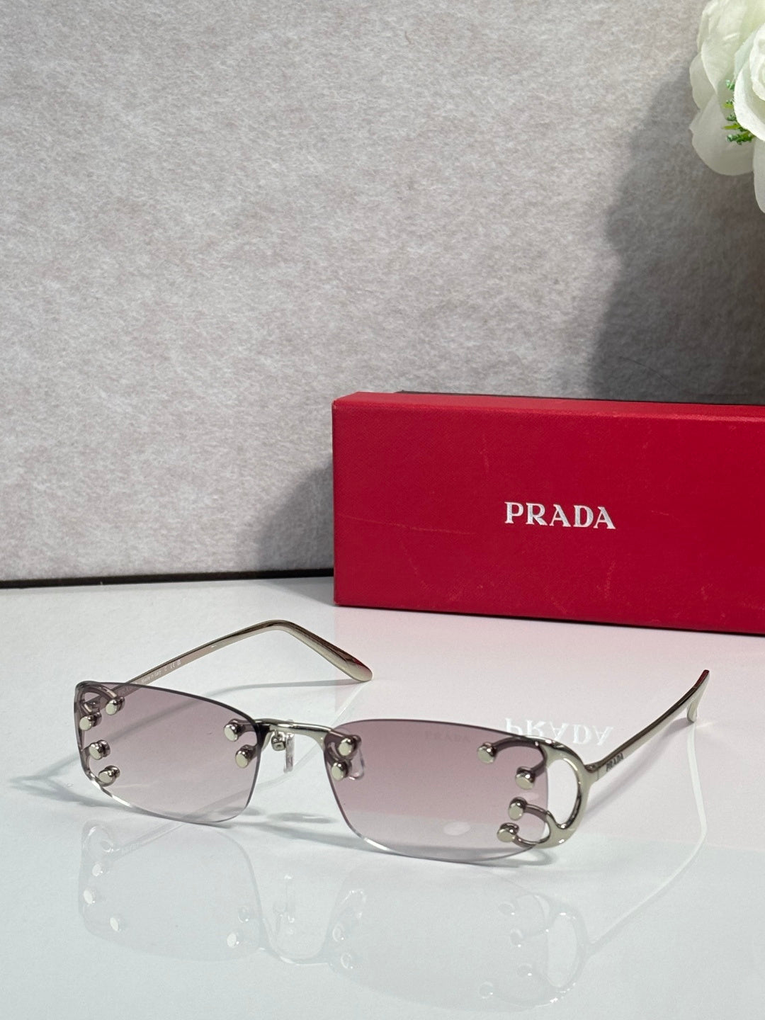 Eyeglasses by Prada with light pink lenses and silver frame, studded detailing on hinges