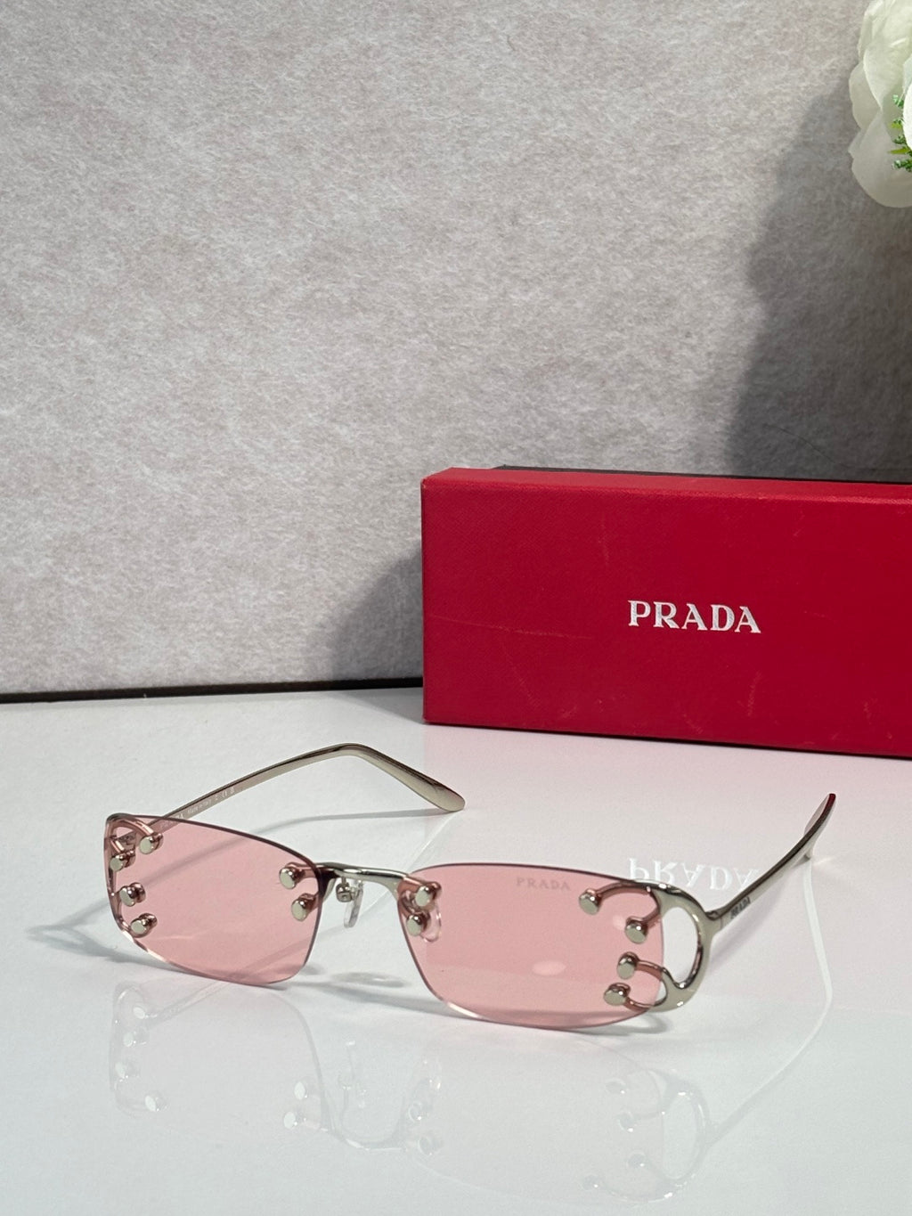 Eyeglasses by Prada with pink-tinted lenses and silver frame, studded detail at temples