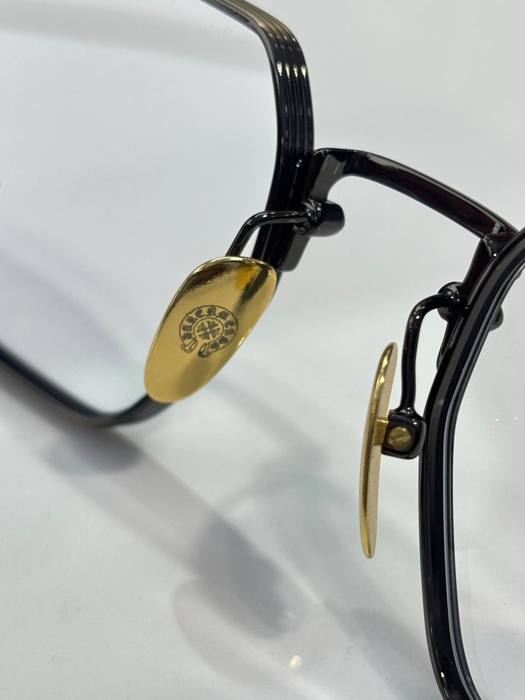 Black eyeglass frame close-up with gold-tone hinge and clear lens