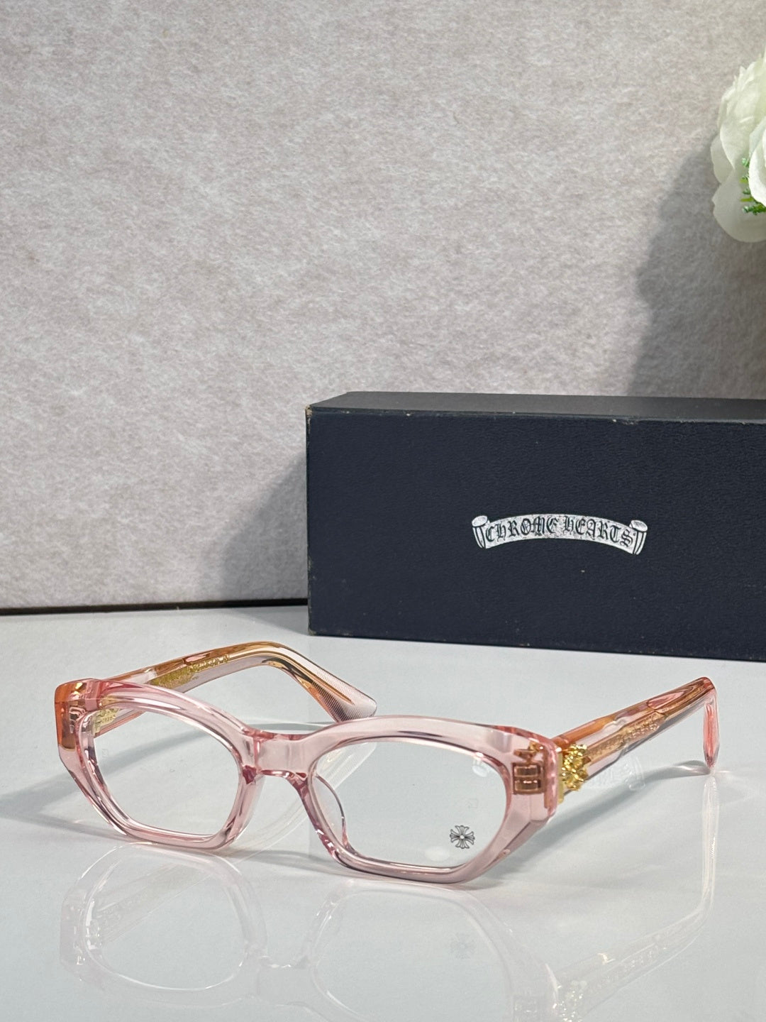 Chrome glasses with pink frame, round-square clear lenses, and decorative hinges.