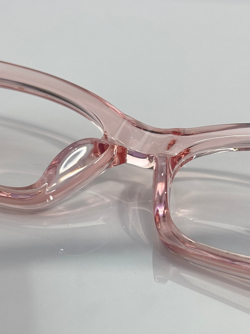 Chrome glasses close-up: pink translucent frame, curved bridge, clear lenses.