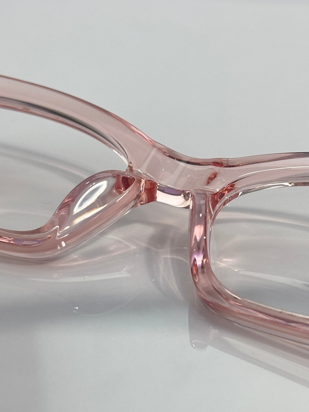 Chrome glasses close-up: pink translucent frame, curved bridge, clear lenses.