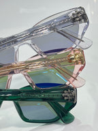 Stacked clear glasses frames with blue, green, and gold-tinted lenses