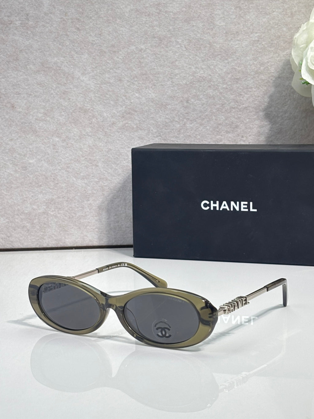 Chanel sunglasses with olive-green frames and dark lenses; Chanel logo on metal temple
