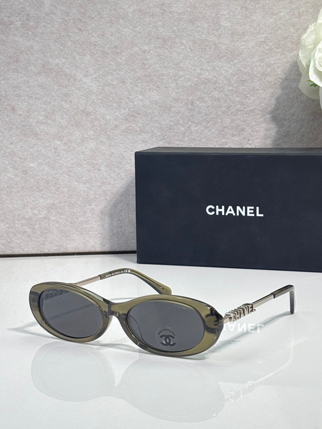 Chanel sunglasses with olive-green frames and dark lenses; Chanel logo on metal temple