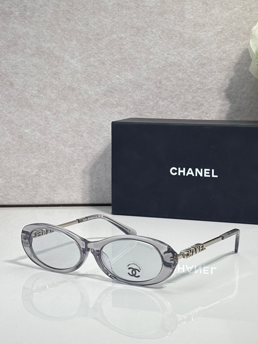 Chanel sunglasses with light gray frames and clear lenses; Chanel logo on metal temple