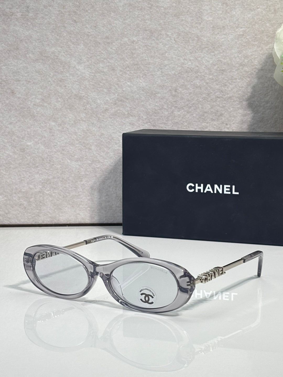 Chanel sunglasses with light gray frames and clear lenses; Chanel logo on metal temple