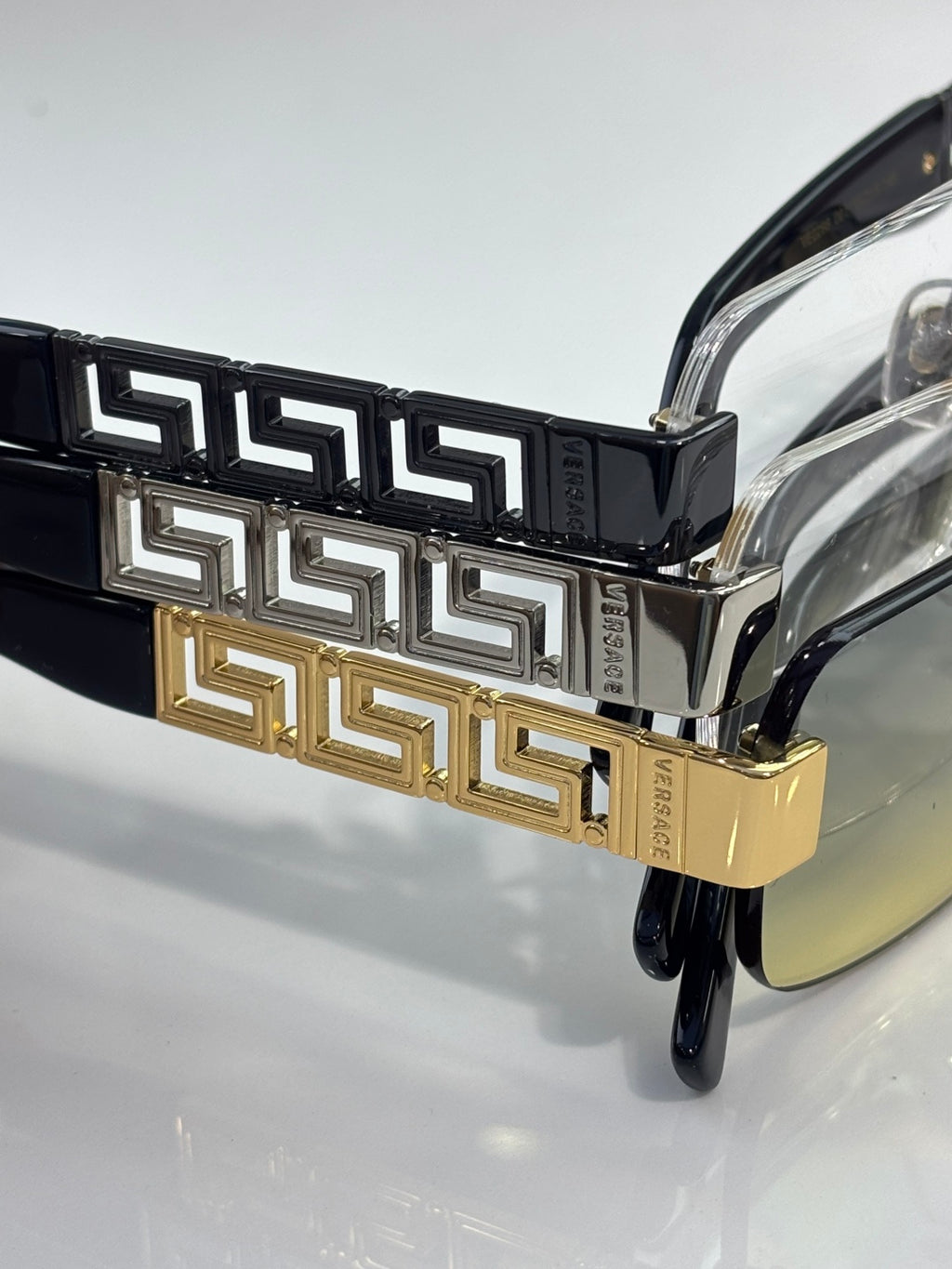 Versace glasses close-up: black temple with gold Greek key band, clear lens