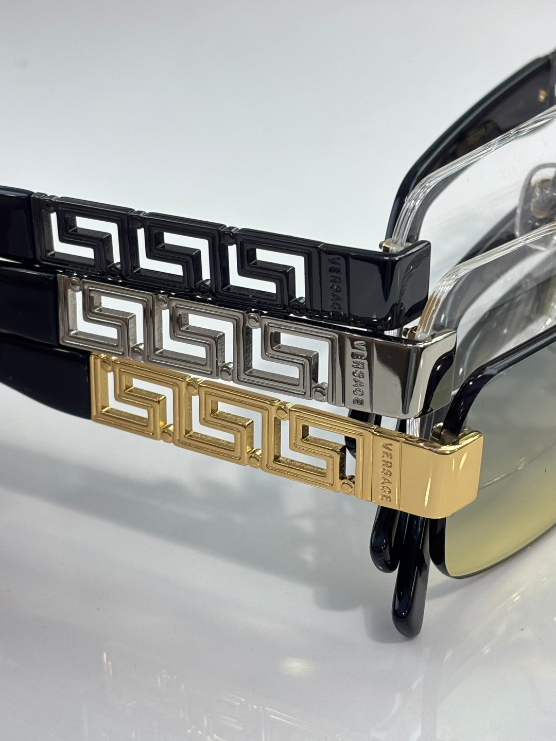 Versace glasses close-up: black temple with gold Greek key band, clear lens