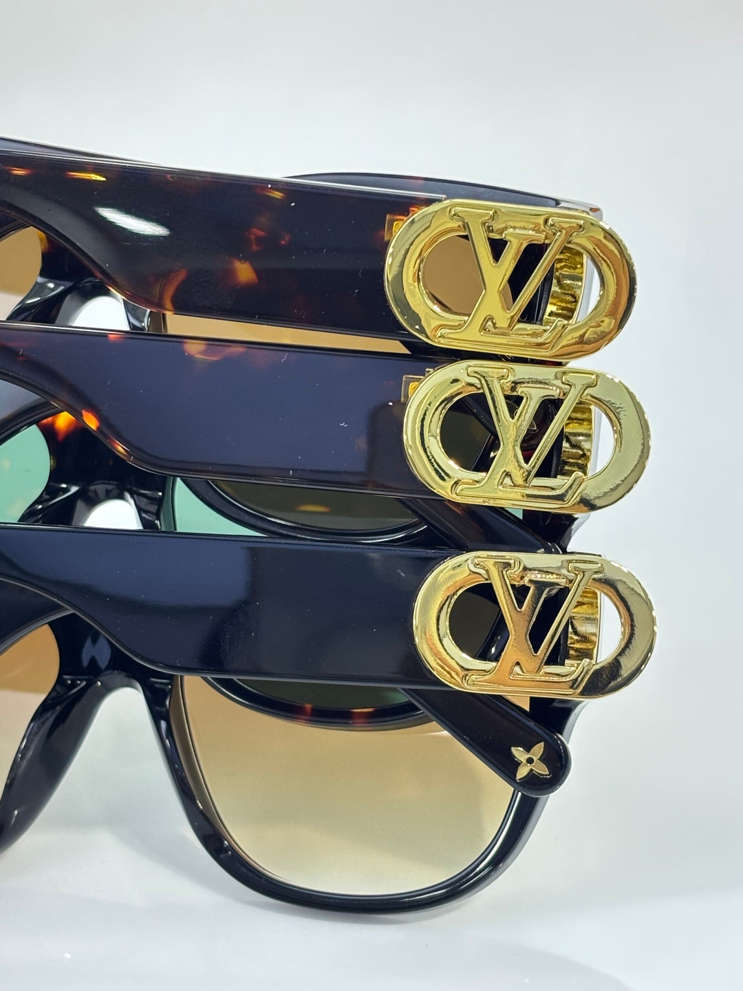 Gold LV logo badges on dark sunglasses front frame, side view