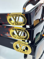 Gold LV emblems on dark sunglasses temple tips, close-up