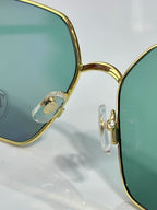 Gold rectangular sunglasses with green lenses, temple hinge detail close-up