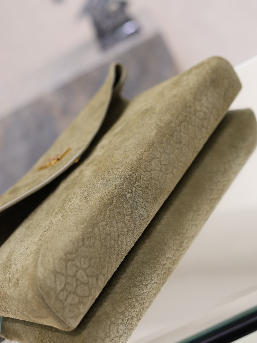 Olive textured leather clutch bag with structured flap and gold monogram on edge