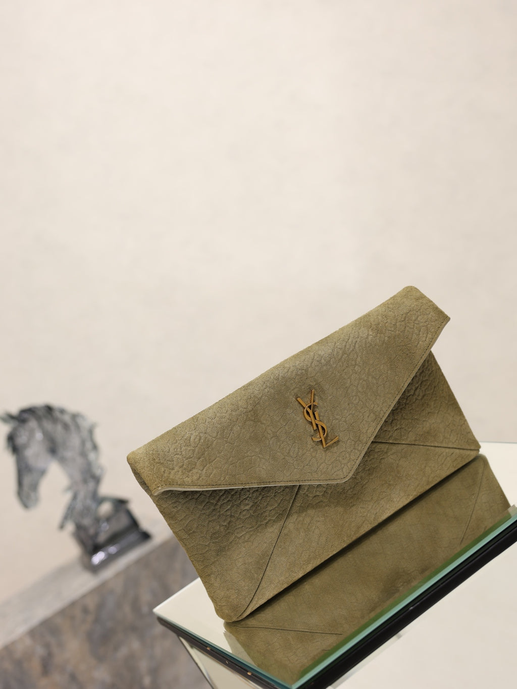 Olive textured leather envelope clutch bag angled on a glass display stand