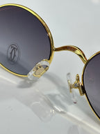 Close-up of Cartier round gold glasses with dark lenses and jeweled hinge