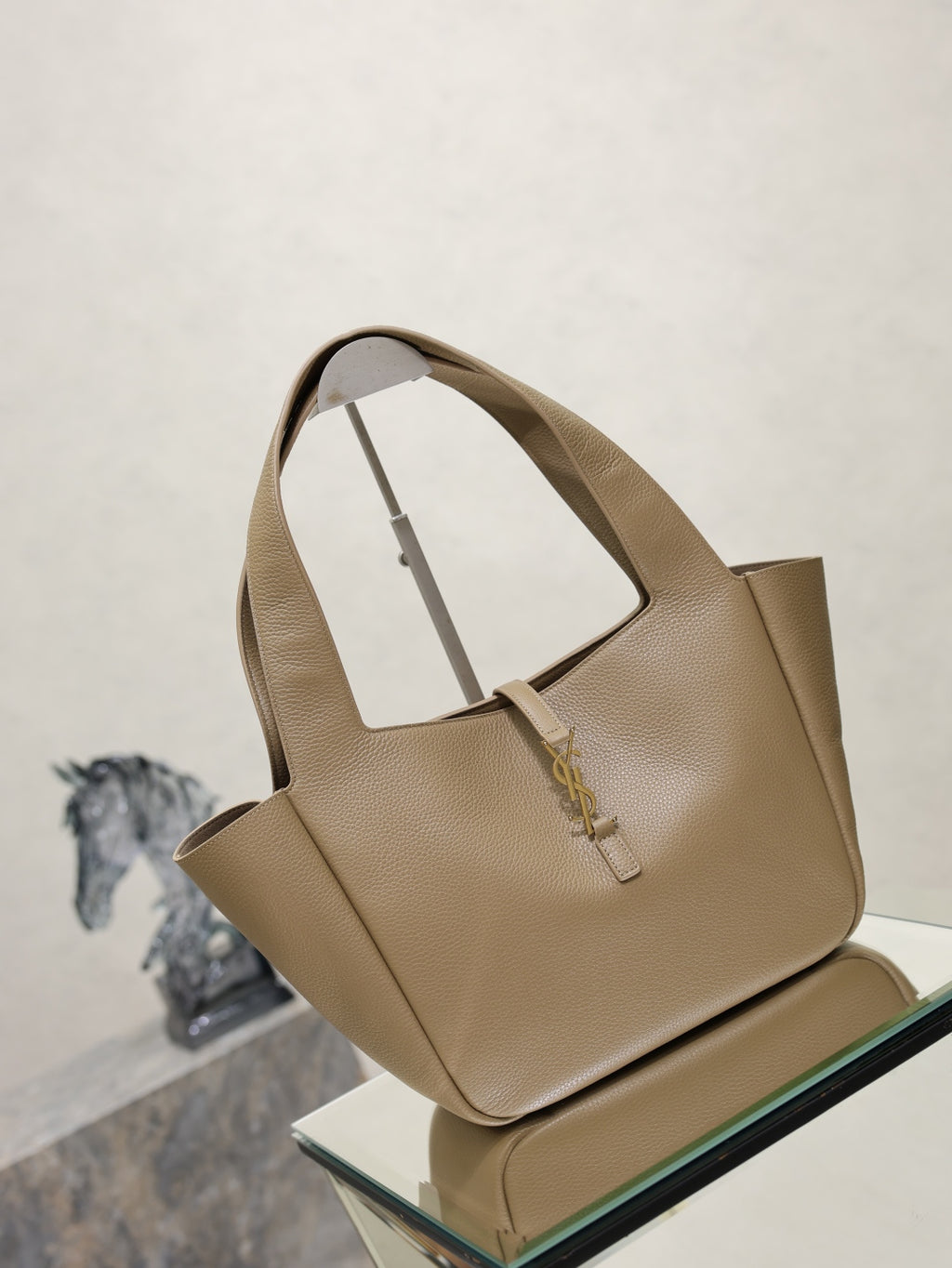 Beige leather tote bag with structured sides and gold logo charm at front