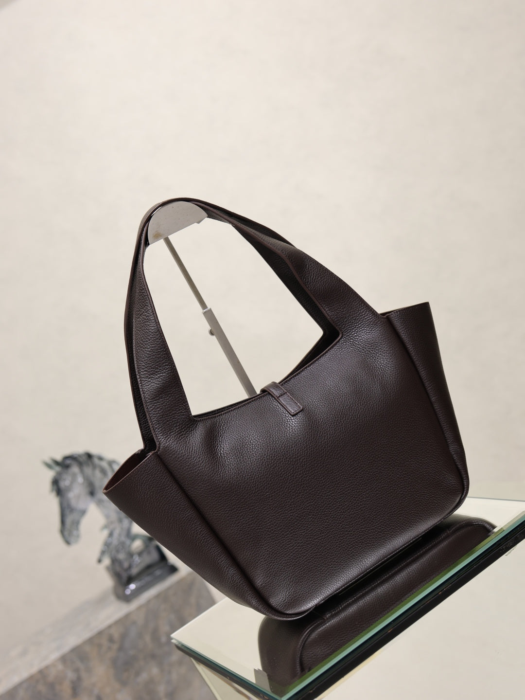 YSL bag tote back/side view in dark pebbled leather on glass display