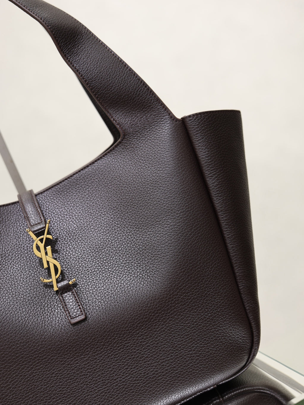 YSL bag side view in dark pebbled leather with gold YSL logo charm strap