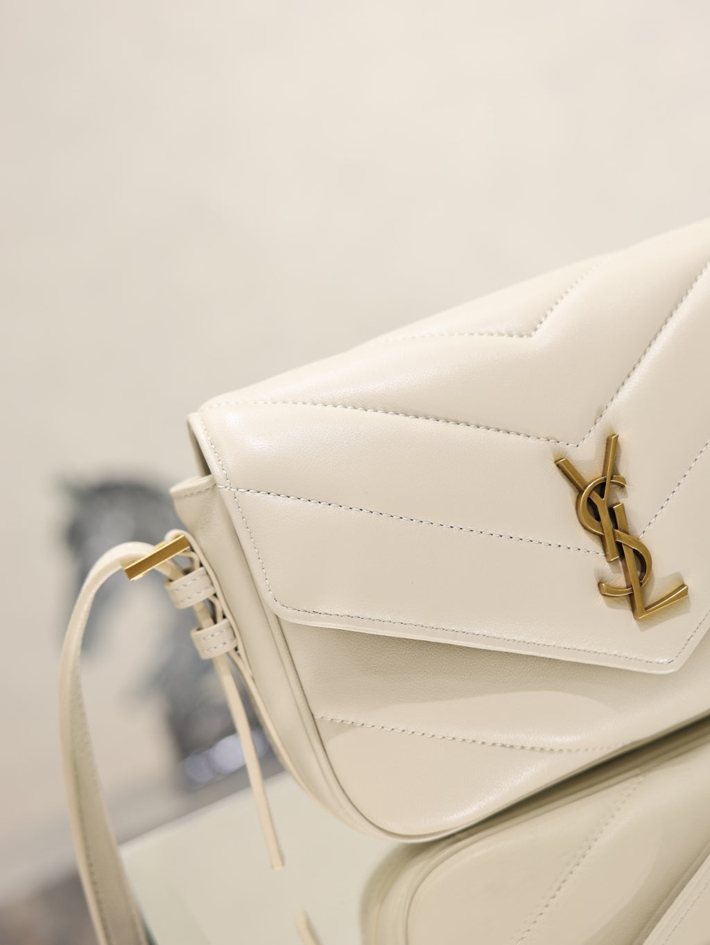 Cream YSL flap bag close-up with gold logo hardware and stitched quilting