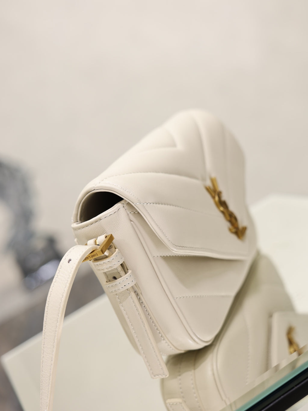 Cream YSL flap bag with strap and gold hardware, shown from rear angle