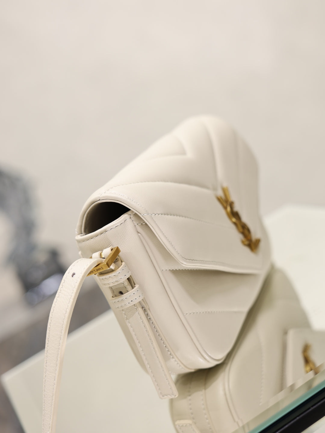 Cream YSL flap bag with strap and gold hardware, shown from rear angle
