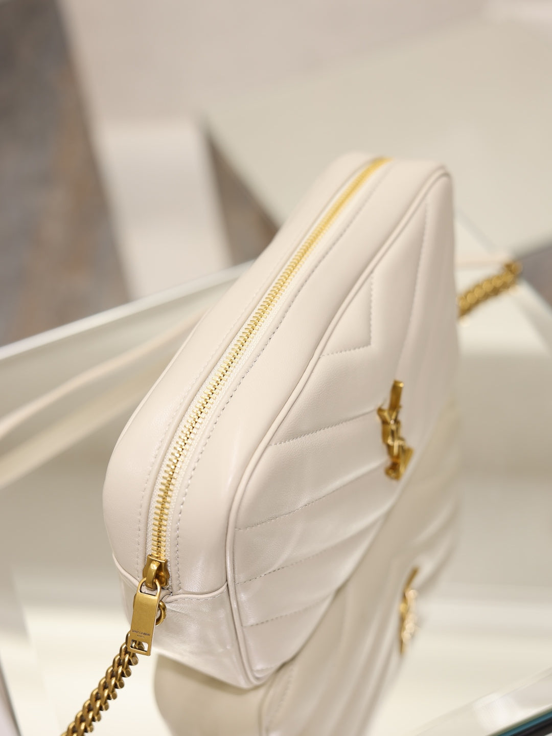YSL cream quilted bag angled view with gold zipper, logo clasp, and chain strap