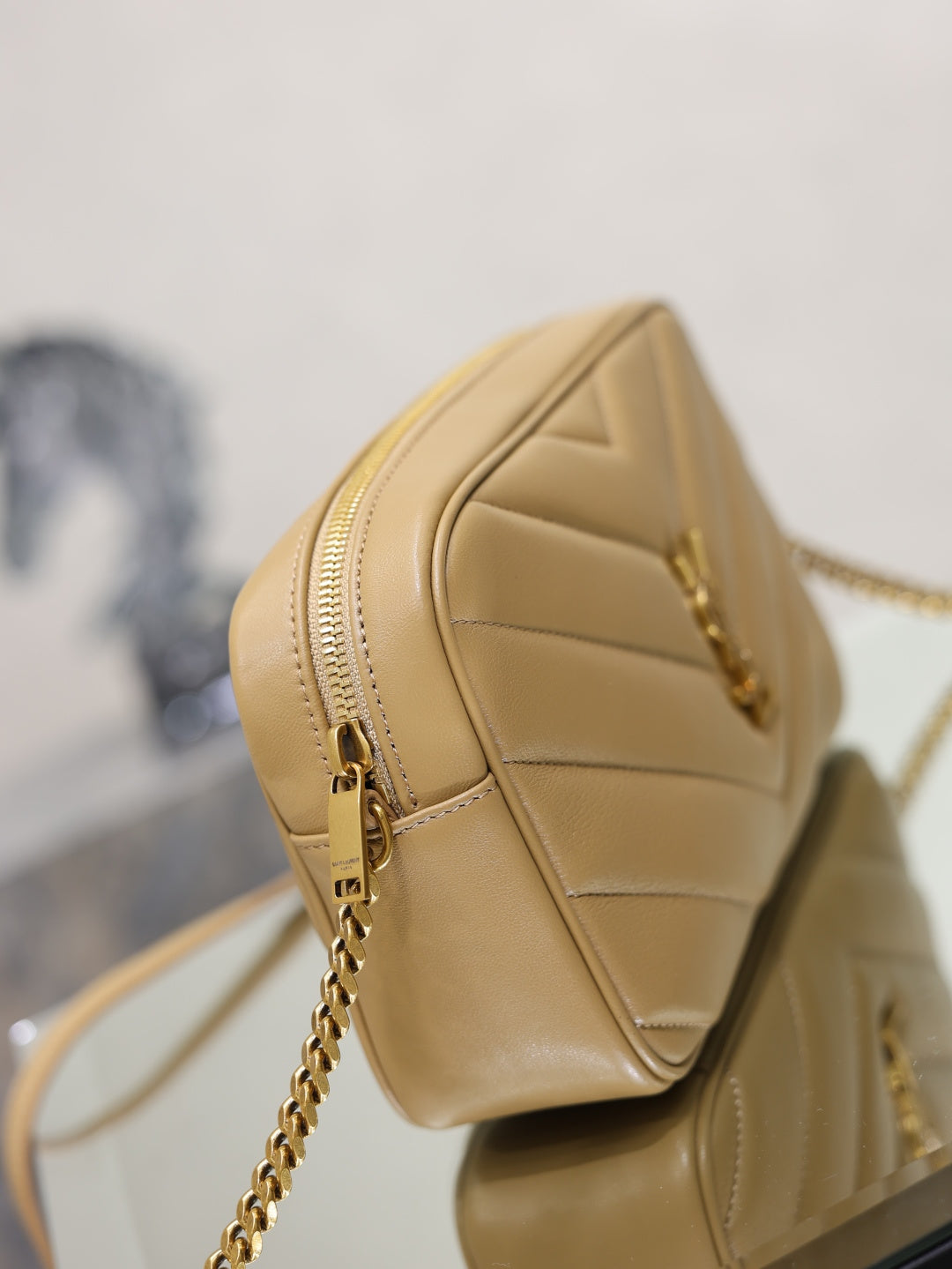 Side view of quilted leather shoulder bag with zip and chain strap, light tan
