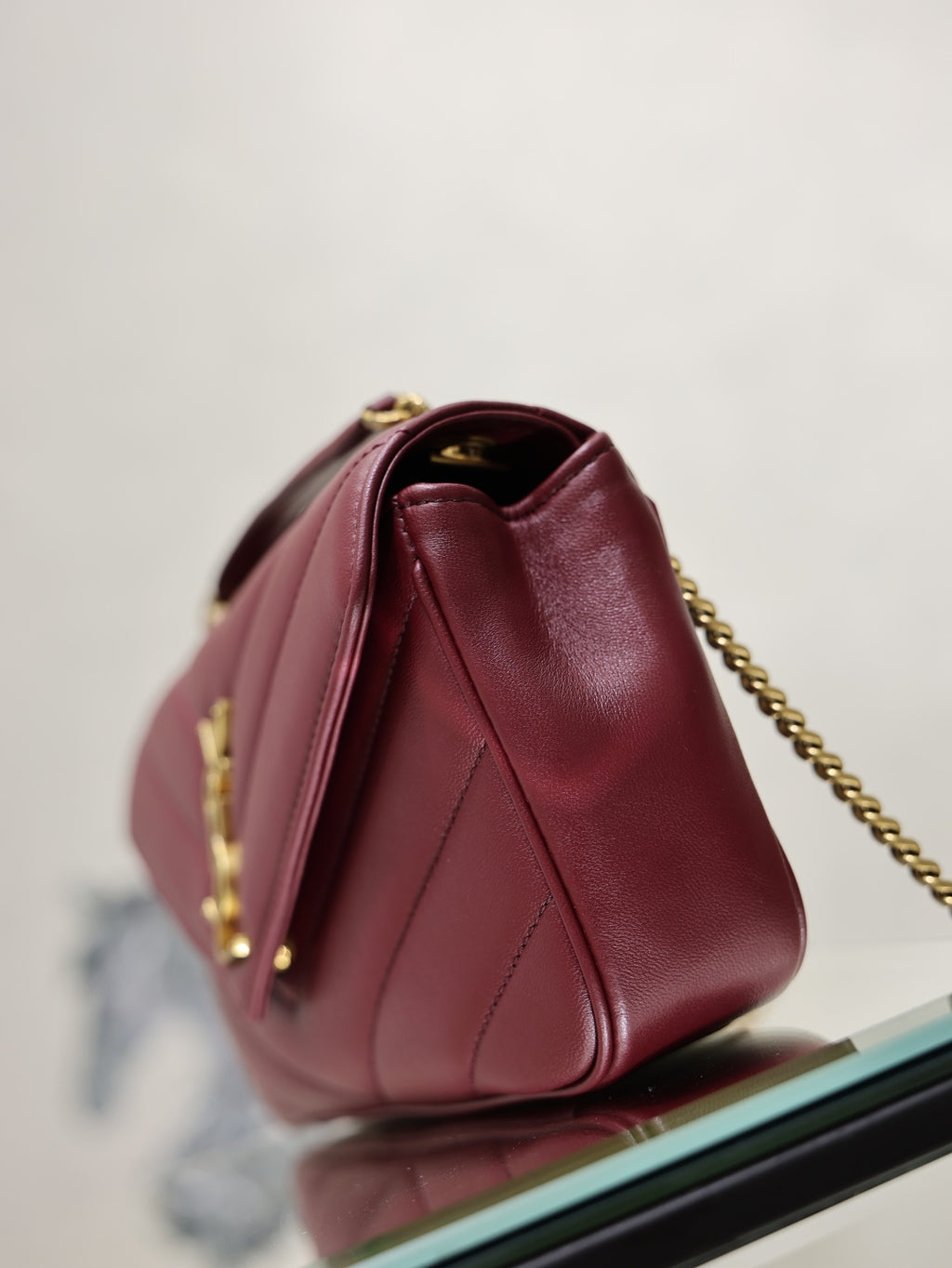 Burgundy quilted shoulder bag with rounded top, gold chain strap, and side seam detail.