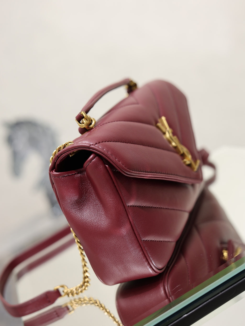 Burgundy quilted shoulder bag with curved flap, gold hardware, and chain strap.