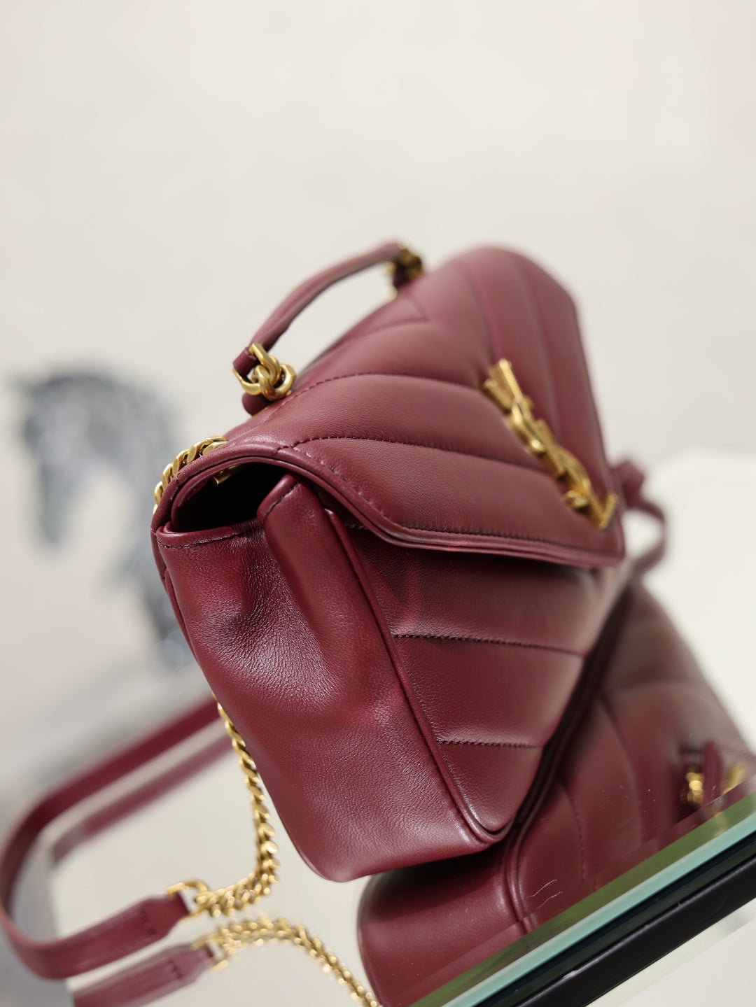 Burgundy quilted shoulder bag with curved flap, gold hardware, and chain strap.