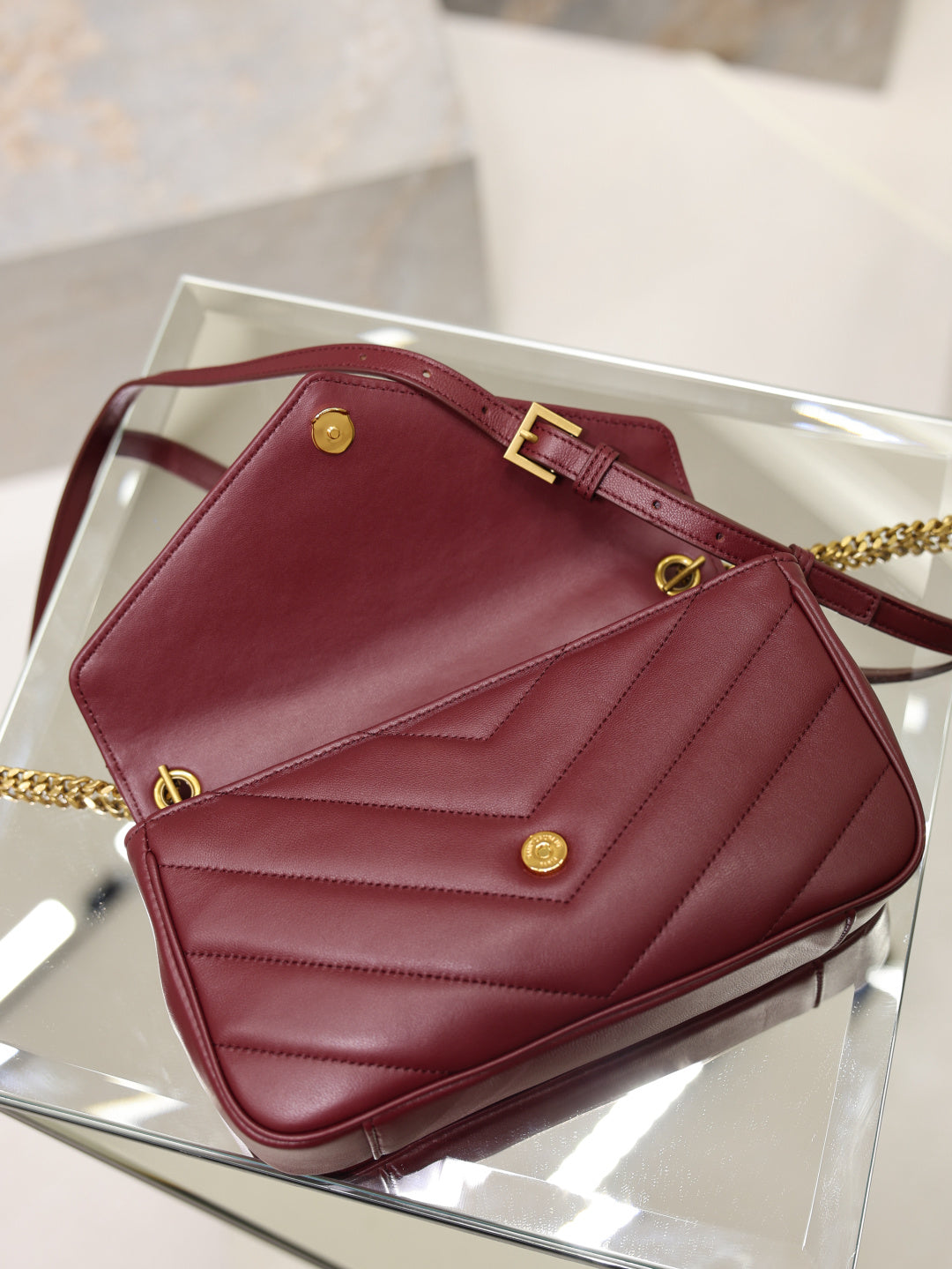 Burgundy quilted shoulder bag with gold buckle strap, front flap, and chain hardware.