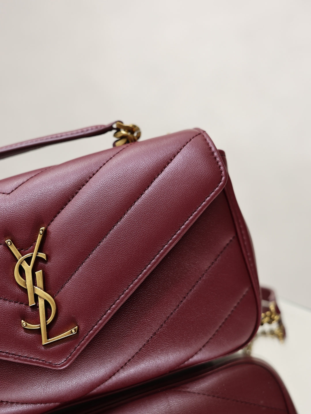 Burgundy quilted shoulder bag detail with gold YSL logo on front flap.