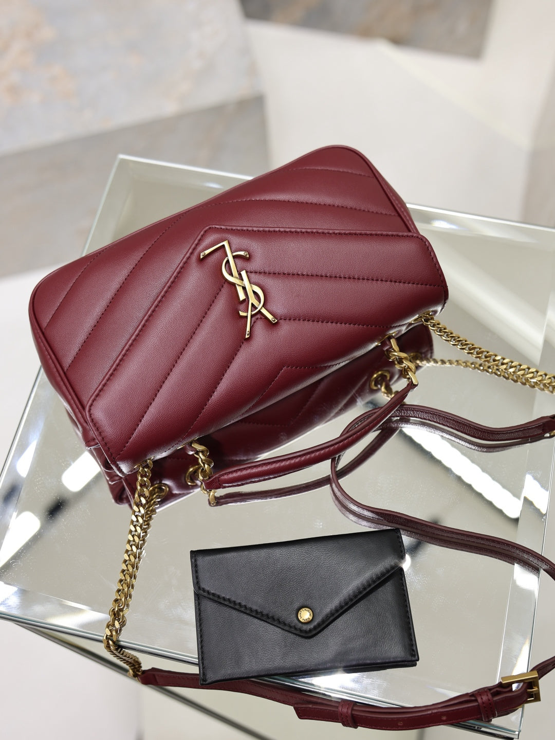 Burgundy quilted shoulder bag with gold YSL logo on flap, chain strap.