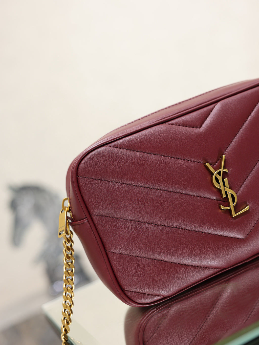 YSL bag corner view in burgundy with gold YSL logo and quilted stitching