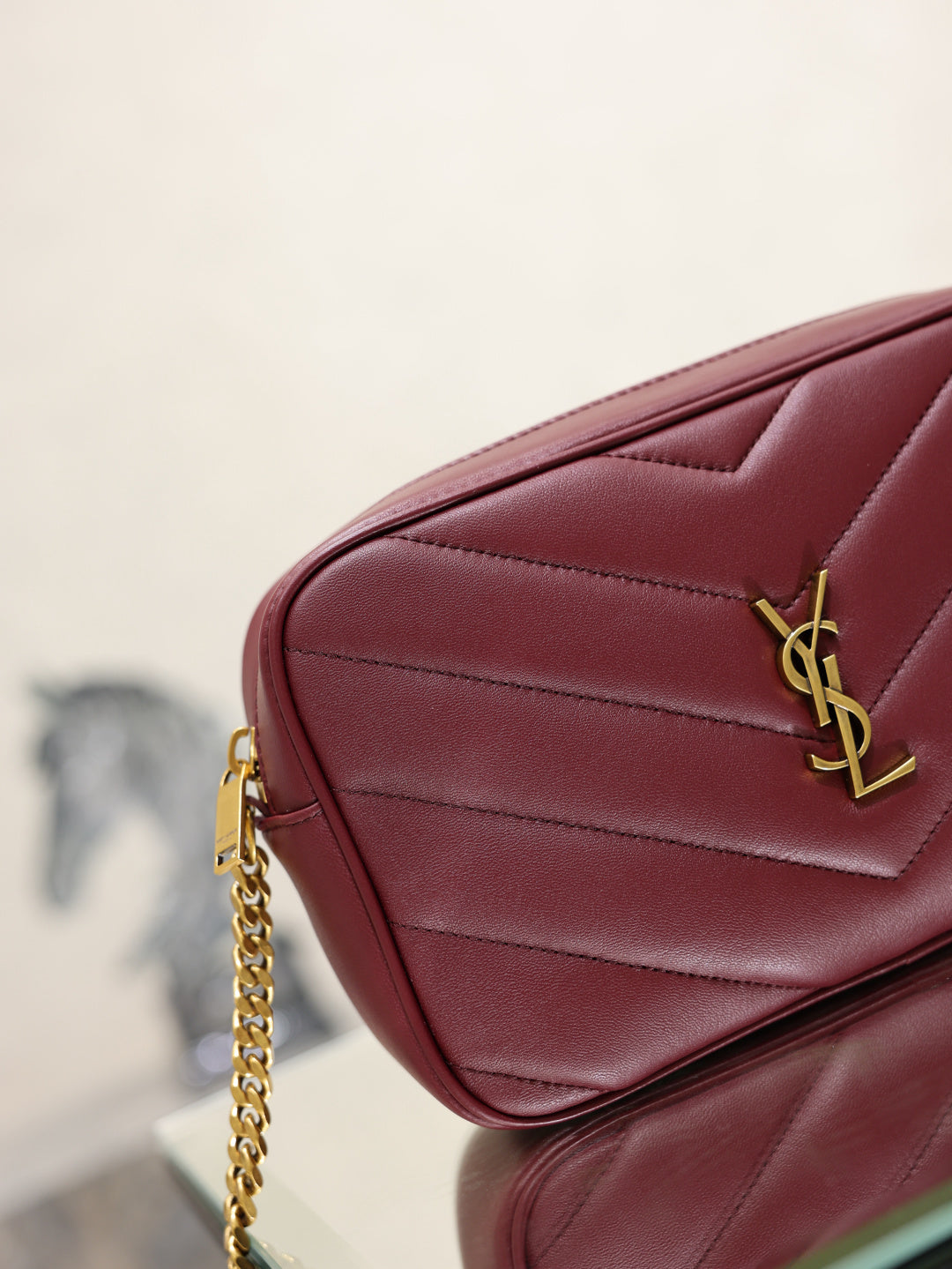 YSL bag corner view in burgundy with gold YSL logo and quilted stitching