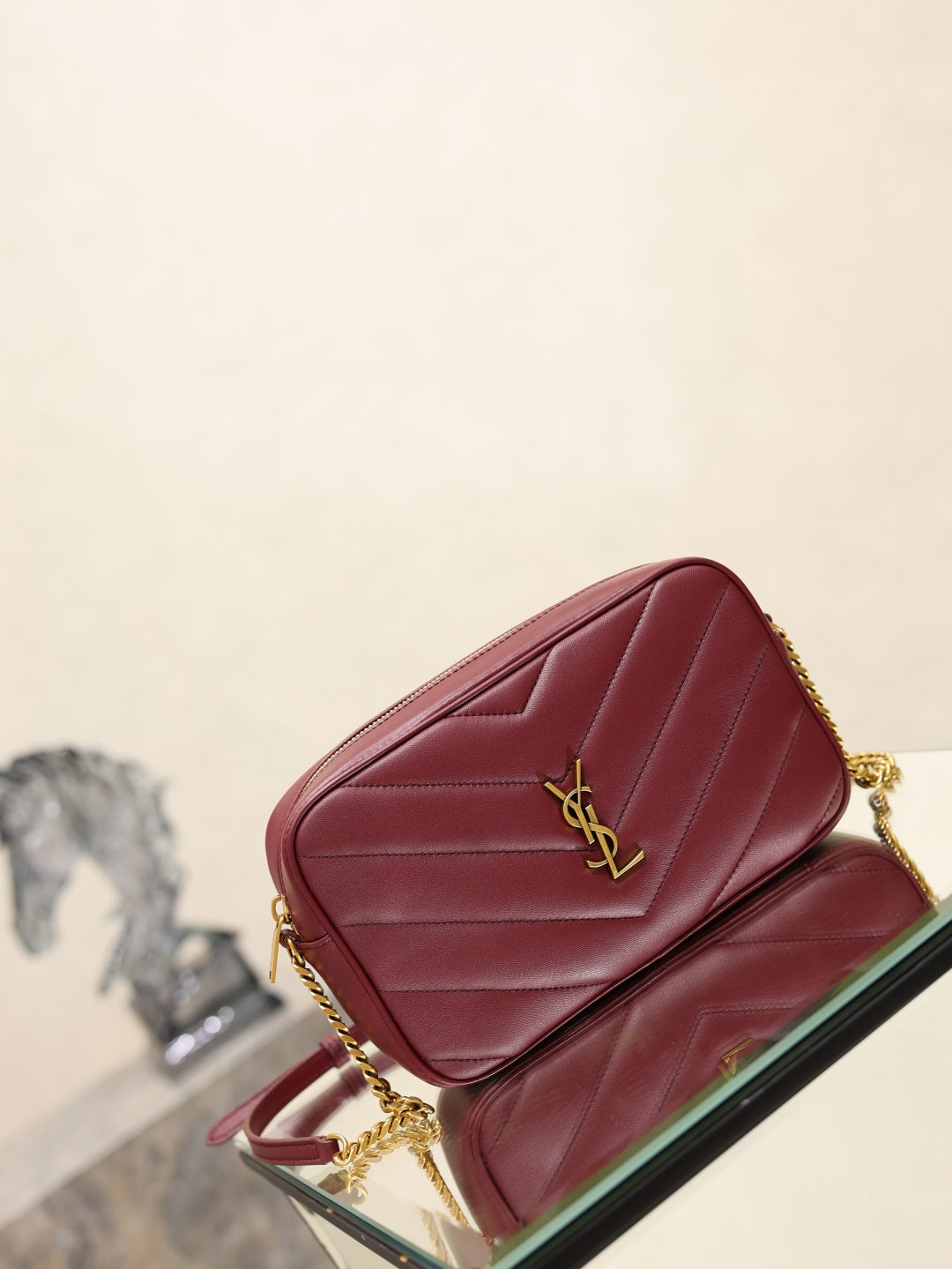 YSL bag with burgundy quilted design, gold YSL logo, and top zip opening