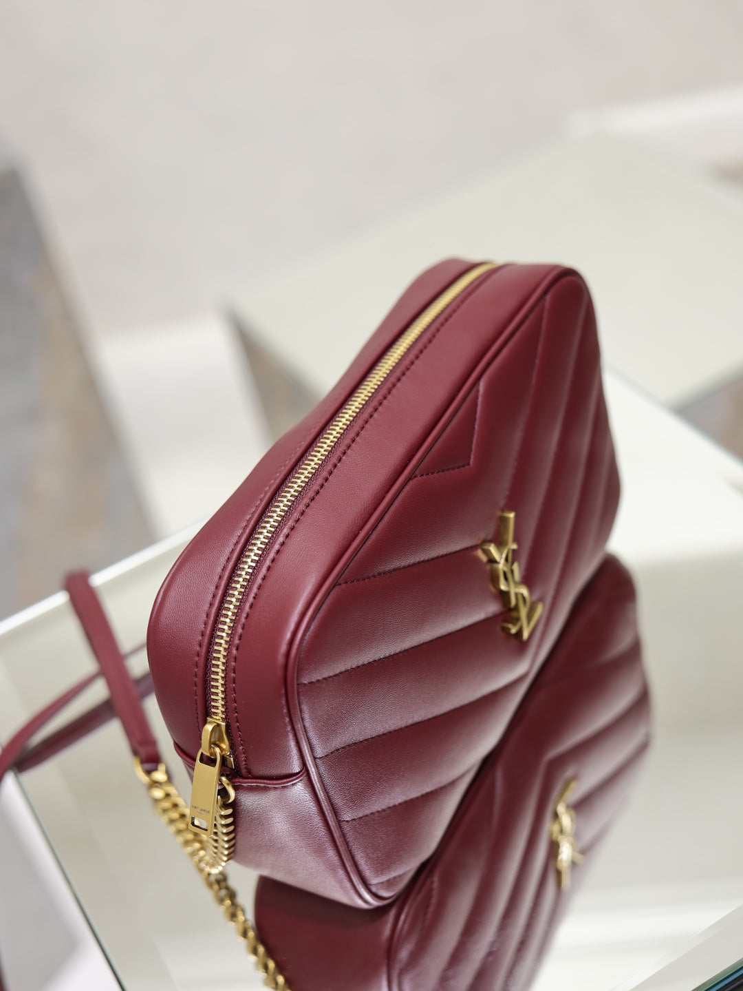YSL bag side profile in burgundy with gold chain, YSL logo, and zip closure