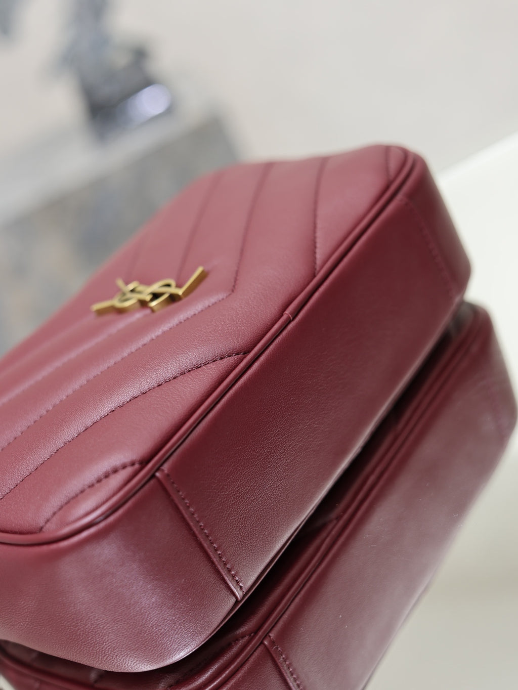 YSL bag close-up in burgundy with gold YSL logo and smooth stitched panels