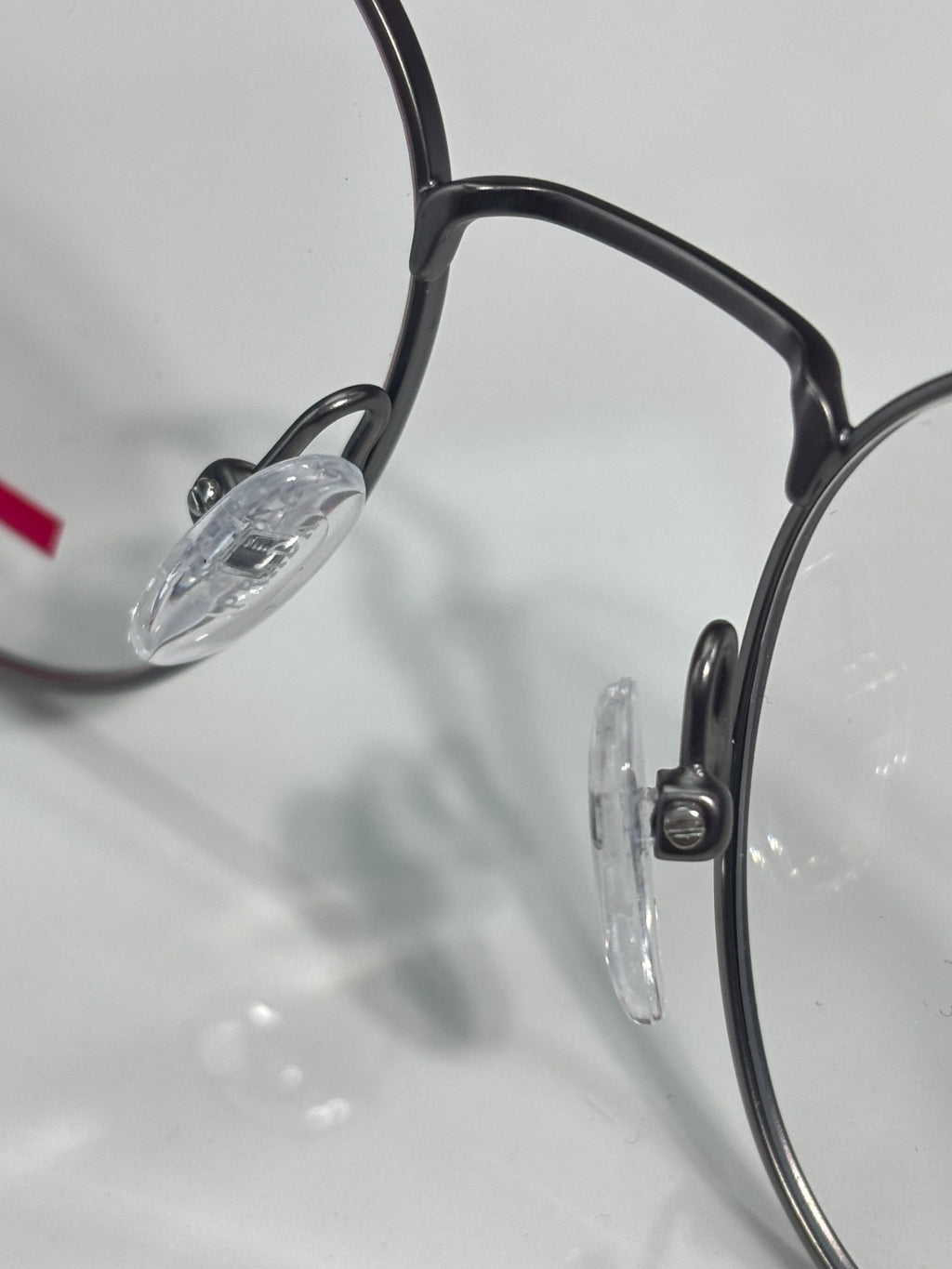 Eyeglasses close-up: dark frame, clear lens, and metal hinge detail.