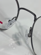 Eyeglasses close-up: dark frame, clear lens, and metal hinge detail.
