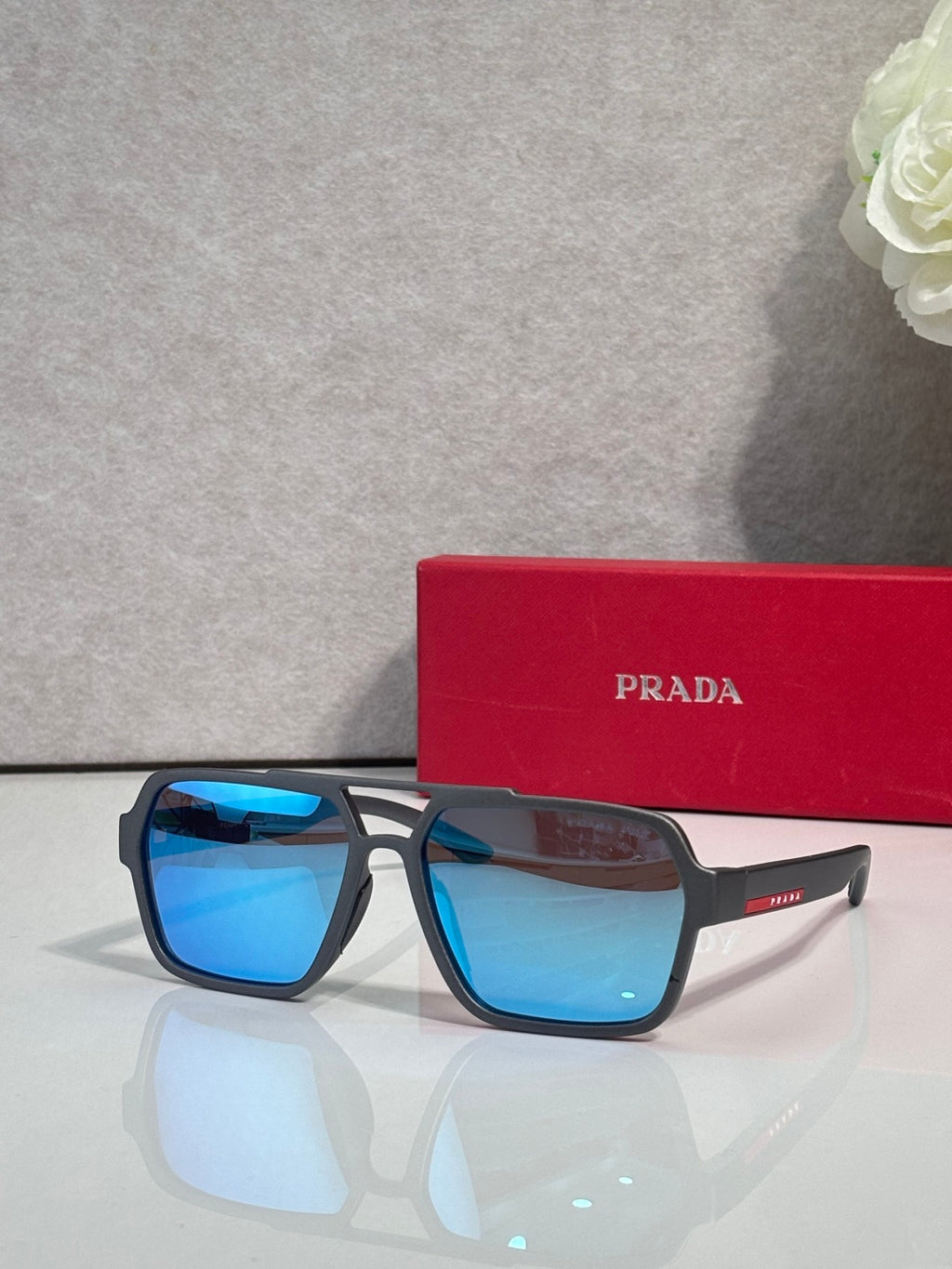 Prada black square sunglasses with blue mirrored lenses, with red Prada case behind