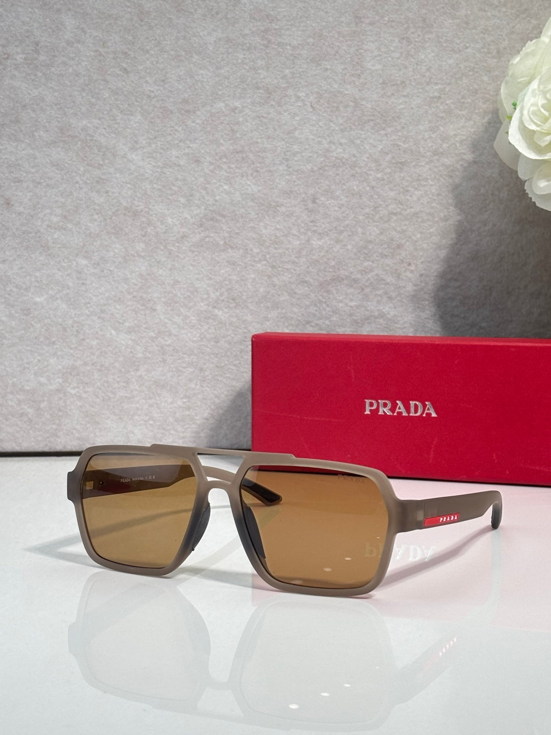 Prada dark sunglasses with tan frames and brown mirrored lenses, red Prada case behind