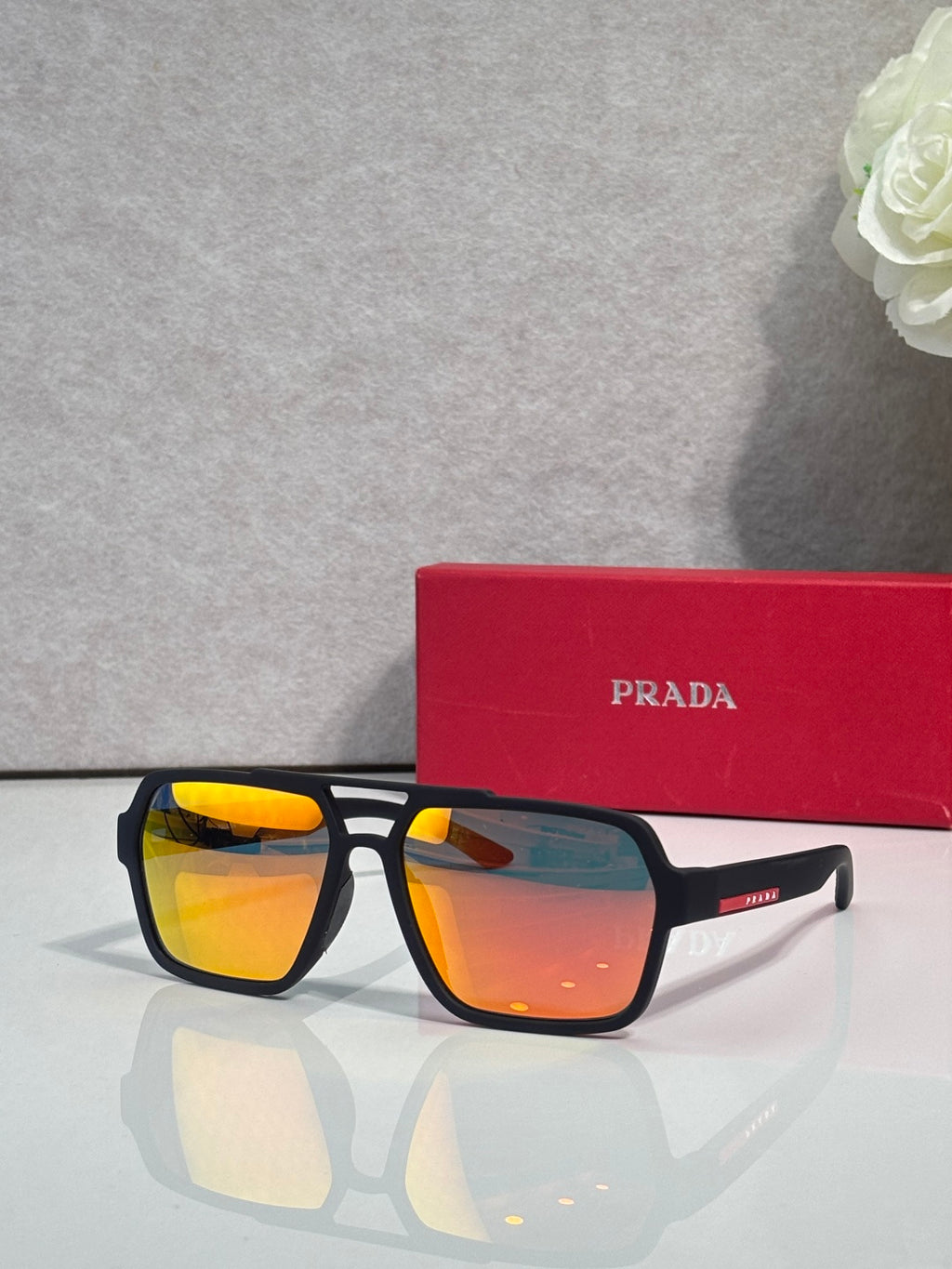 Prada black square sunglasses with orange mirrored lenses, with red Prada case behind