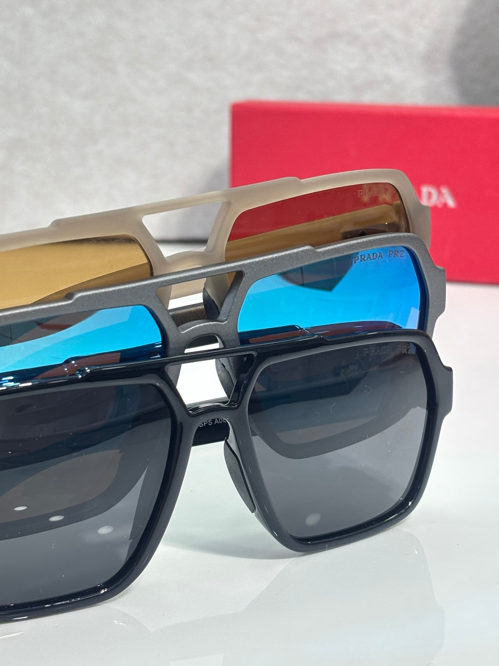 Prada sunglasses pair with beige frames and blue lenses, stacked over dark frames
