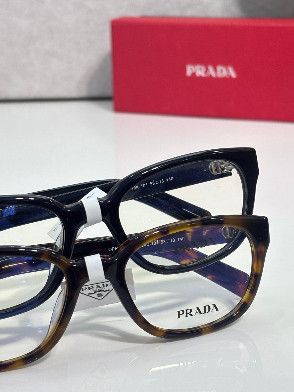 Prada glasses with mix of black and tortoise frames, clear lenses, and PRADA logo.