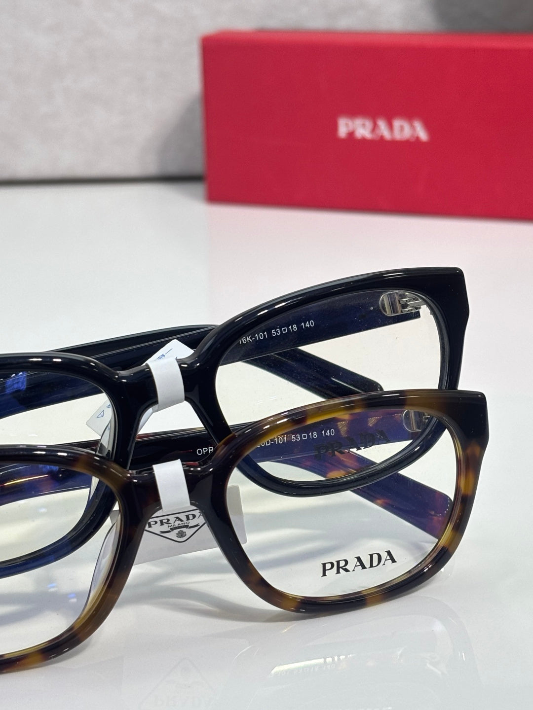 Prada glasses with mix of black and tortoise frames, clear lenses, and PRADA logo.